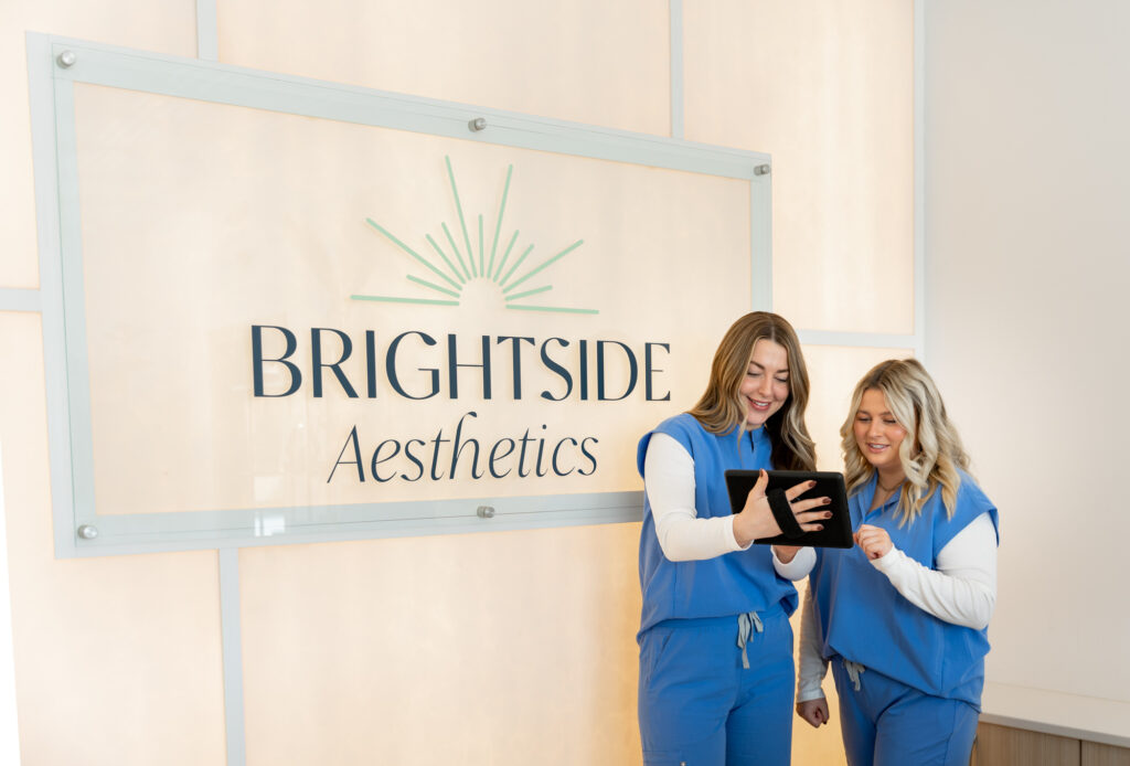Two female providers at Brightside Aesthetics help a patient check in for a consultation to learn more about Emsella near West Des Moines.