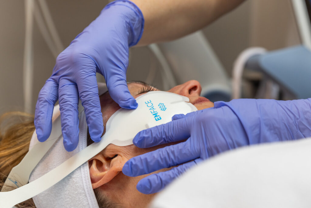 Close up of gloved hands applying Emface facial contouring applicators to a woman's cheeks.